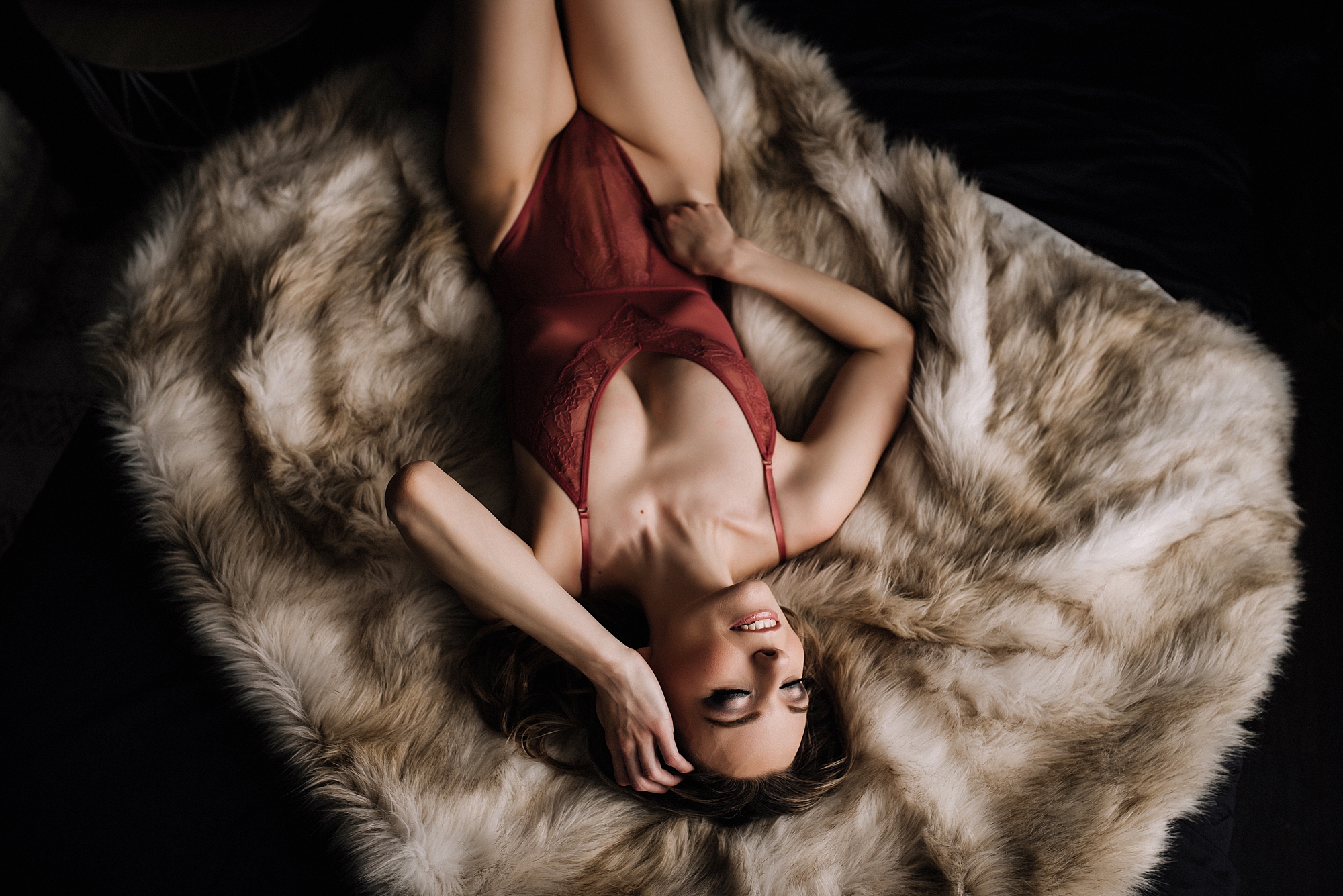 woman posing on fur blanket playing with her hair and tugging on her bodysuit